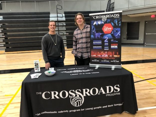 Crossroads Program representatives standing at outreach table with informational display about teen addiction recovery and sobriety support services